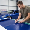 Technicus die op een werkbank een strook matte blauwe ORACAL 970RA carwrapfolie snijdt