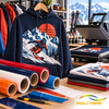 Gepersonaliseerde hoodie met skiedersmotief bedrukt met POLI-FLEX TURBO flexfolie naast een hittepers en gekleurde rollen